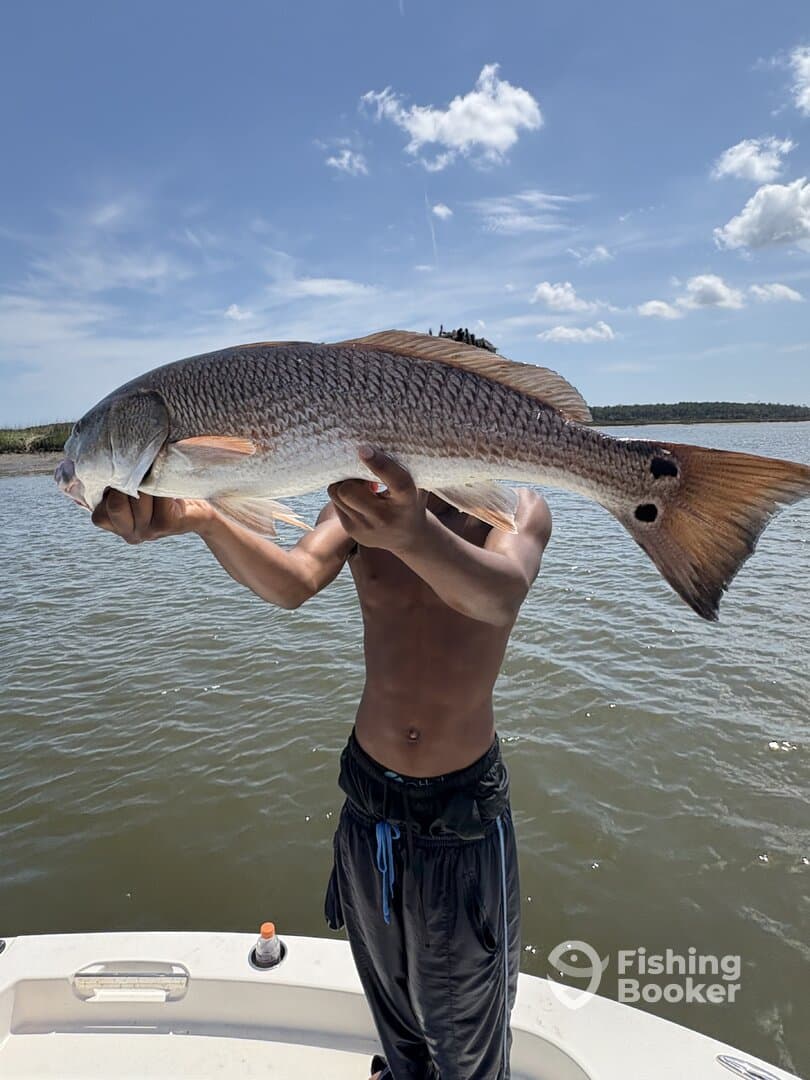 A young angler proudly displaying a large Redfish while fishing on a sunny day.
