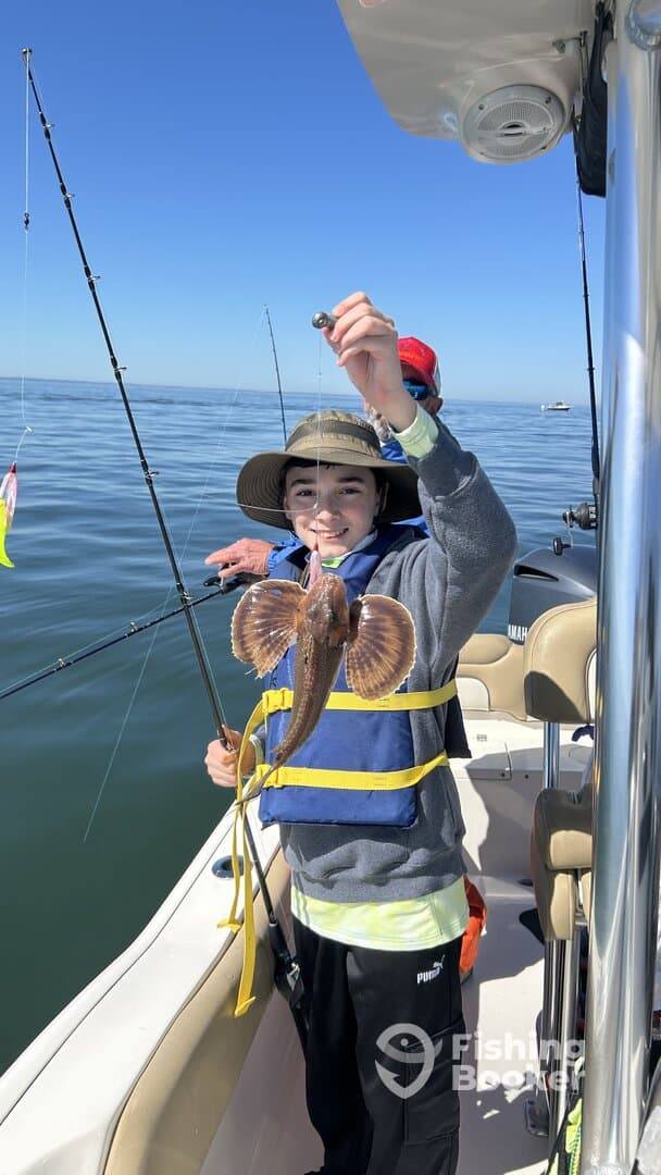 A young angler proudly displaying a caught fish while fishing on a boat in calm waters.