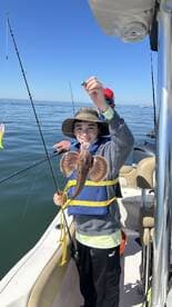 A young angler proudly displaying a caught fish while fishing on a boat in calm waters.