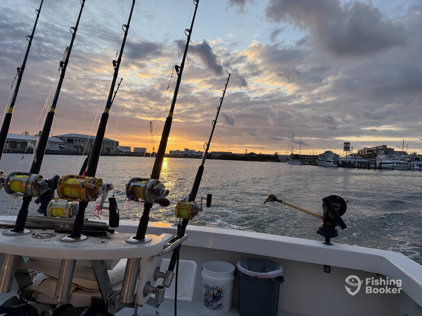 A scenic view from inside a fishing boat, showcasing multiple fishing rods and reels against a beautiful sunset backdrop.