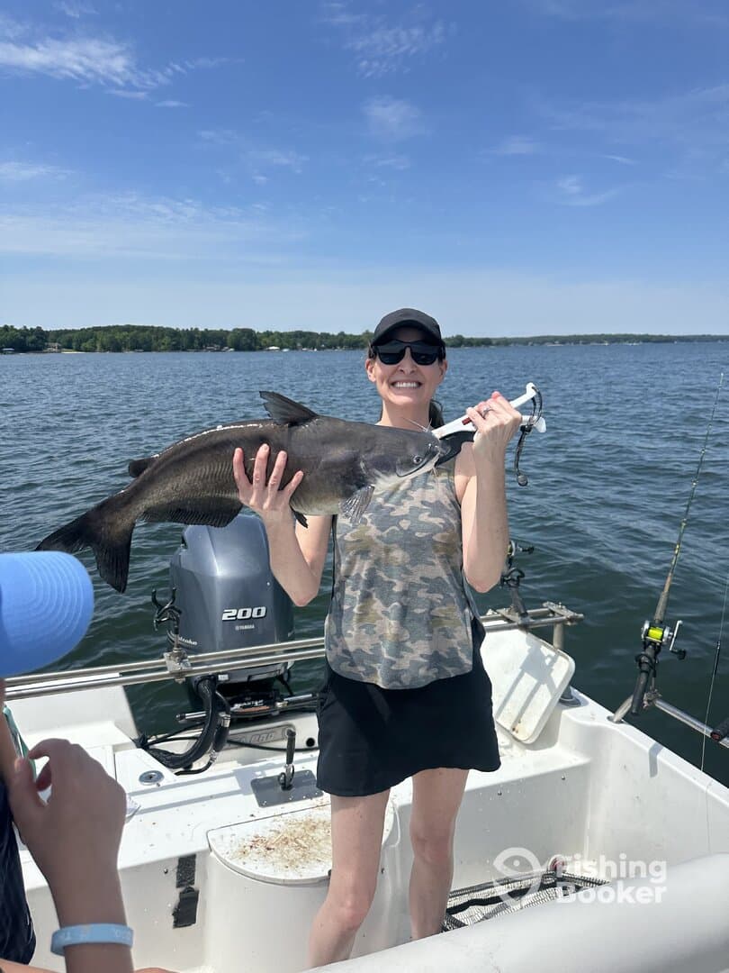 A happy angler proudly displaying a large catfish while fishing on a sunny day, surrounded by family on a boat.