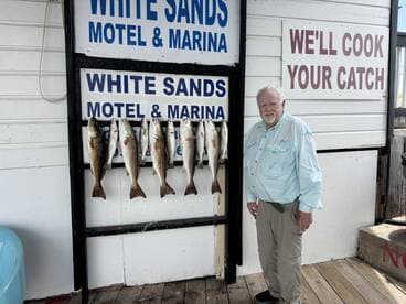 An angler proudly stands next to a display of freshly caught Speckled Trout at the White Sands Motel & Marina, showcasing a successful fishing trip.