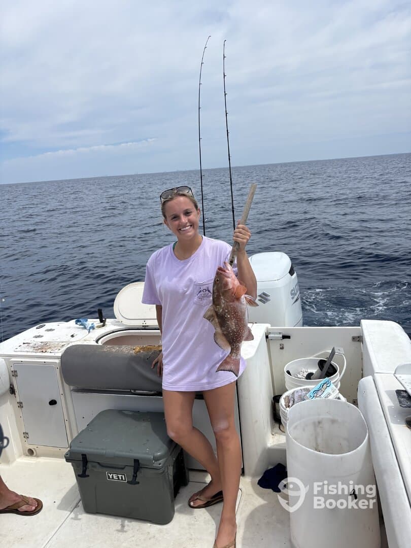A young woman proudly displaying a caught Red Snapper while fishing on a boat in open waters.