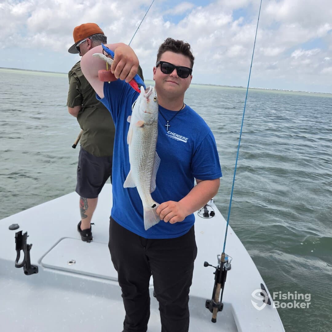 A young angler proudly displaying a caught Redfish while fishing on a boat in coastal waters.
