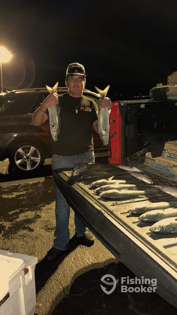 A young angler proudly displaying two large fish after a successful night fishing trip, with several more fish laid out in the truck bed.