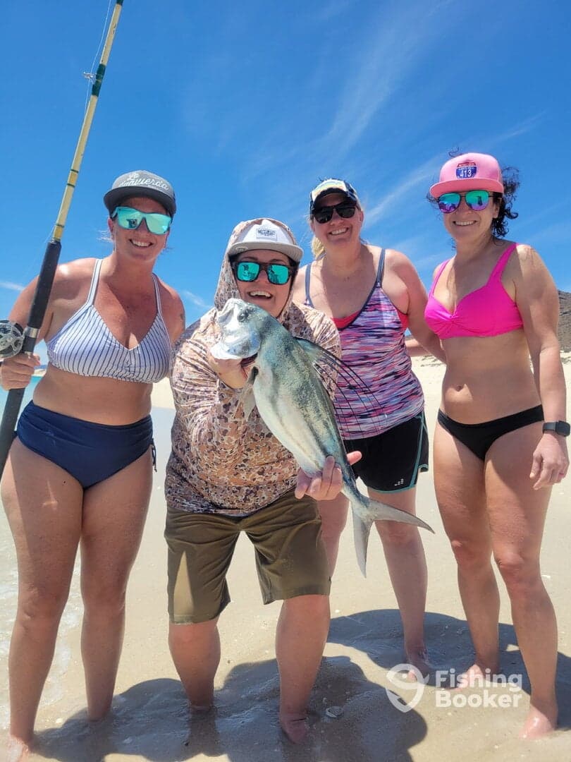 A group of four women proudly displaying a large fish on the beach, enjoying a fun day of fishing together.