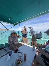 A group of anglers enjoying a fishing trip on a boat, with one person actively reeling in a catch while others relax and enjoy refreshments.