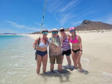 A group of four anglers celebrating a successful catch of a large fish on a sunny beach, showcasing a fun day of fishing in a tropical setting.