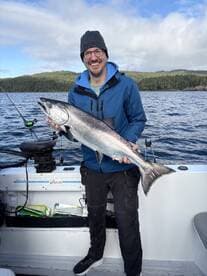 Angler proudly displaying a large Salmon while fishing in a scenic coastal environment.