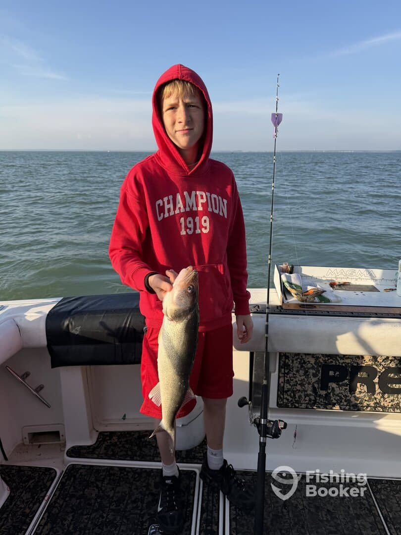 A young angler proudly displaying a sizable Walleye while fishing on a boat, showcasing a beautiful day on the water.