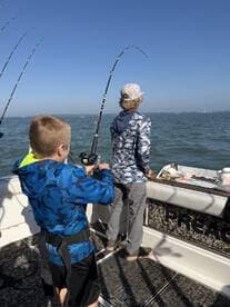 Two young anglers actively fishing on a boat, with rods bent and lines in the water, enjoying a day on the Gulf Coast.