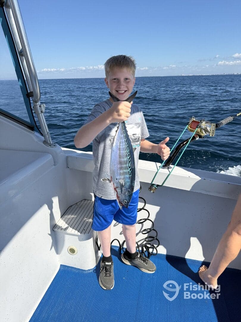 A young angler proudly displaying his catch, a small fish, while aboard a fishing boat in open waters.