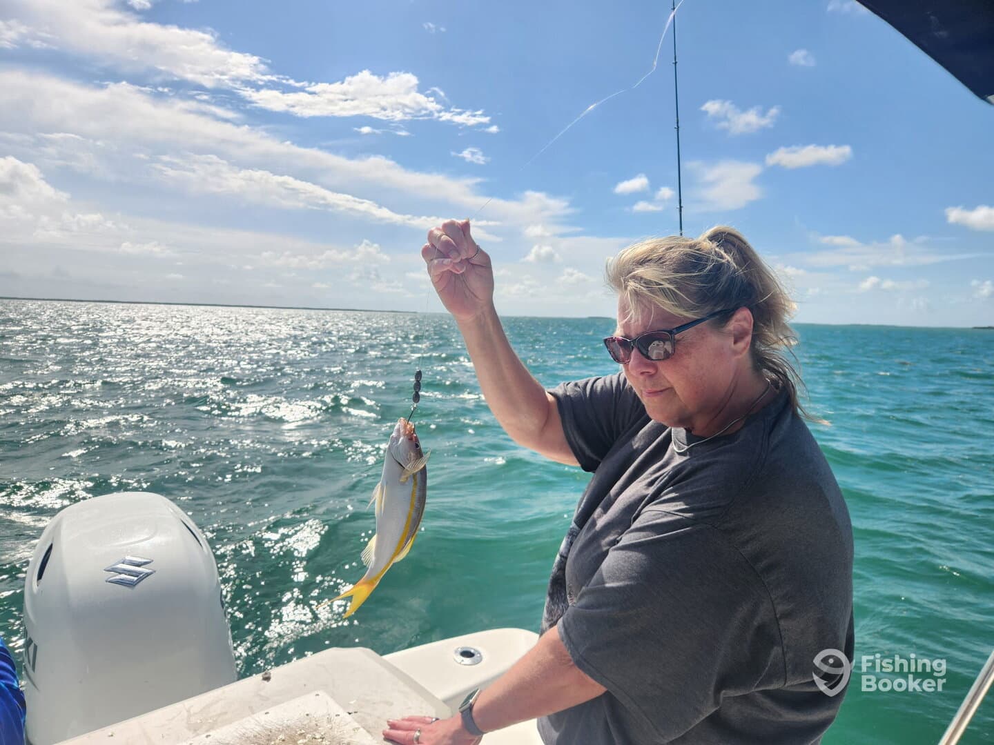 A woman reeling in a small fish while fishing on a boat in sunny waters, showcasing the excitement of the catch.