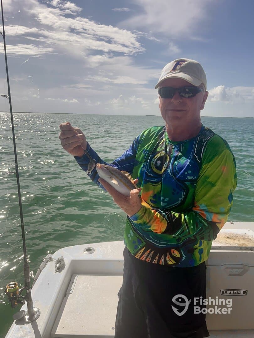 An angler proudly displaying a freshly caught fish while fishing on a boat in sunny waters.