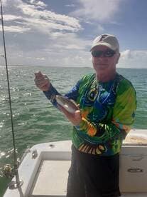 An angler proudly displaying a freshly caught fish while fishing on a boat in sunny waters.