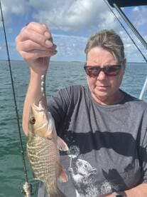 An angler proudly displaying a freshly caught Snapper while fishing on a sunny day.