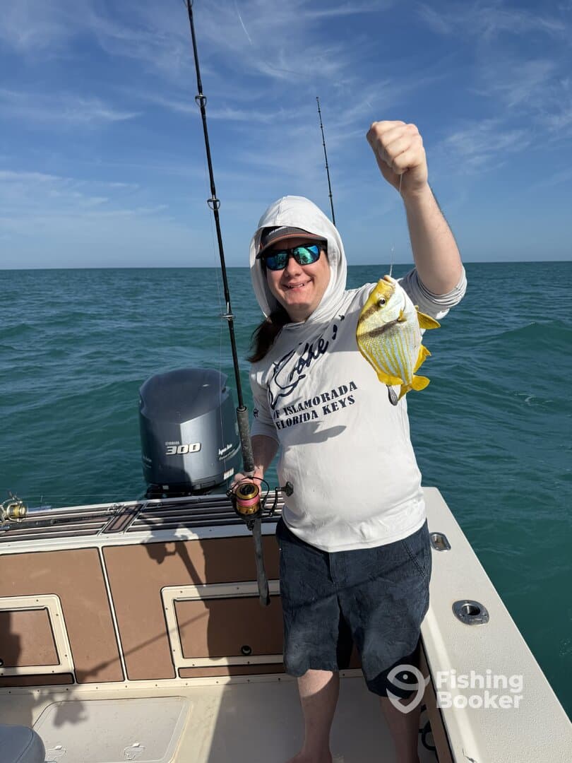 Angler proudly displaying a colorful Yellowtail Snapper while fishing on a boat in the Florida Keys.