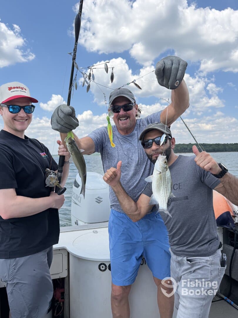 Three anglers proudly displaying their catch, including a striped bass, while fishing on a sunny day.