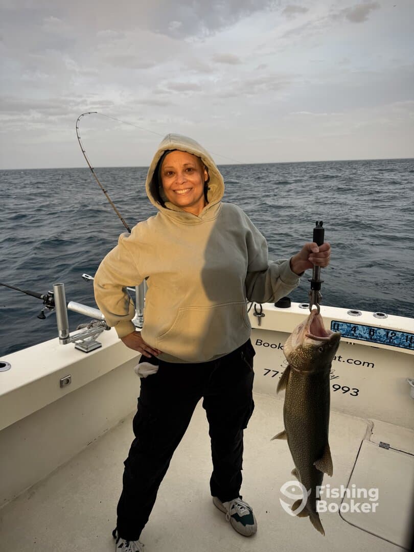 Angler proudly displaying a large Lake Trout while fishing on a charter boat, showcasing a beautiful day on the water.