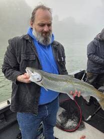 Angler holding a large Steelhead trout while fishing in a misty river environment.