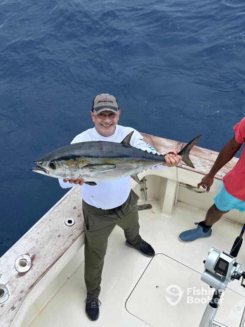 A proud angler displaying a large Tuna on a fishing boat, showcasing a successful deep-sea fishing trip.