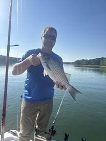 Angler proudly displaying a striped bass while fishing on a calm lake, showcasing a successful day on the water.
