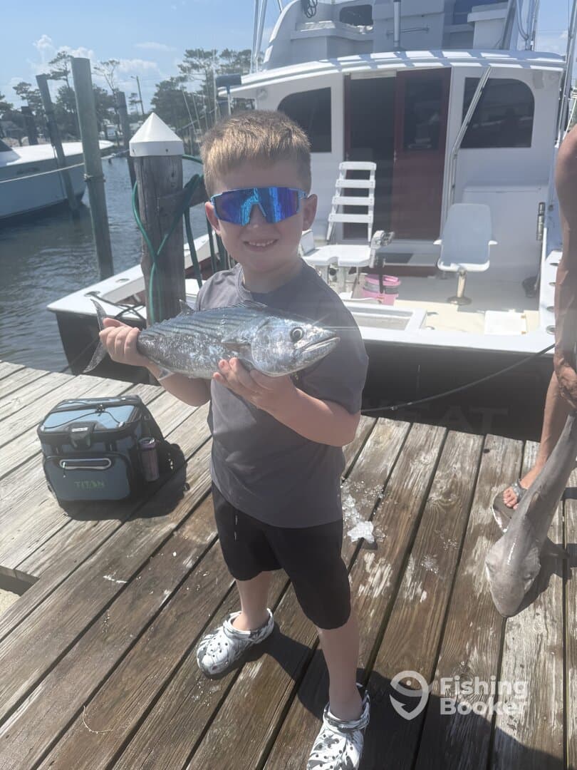 Young angler proudly holding a shiny fish on the dock, showcasing a successful fishing trip.