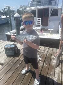 Young angler proudly holding a shiny fish on the dock, showcasing a successful fishing trip.