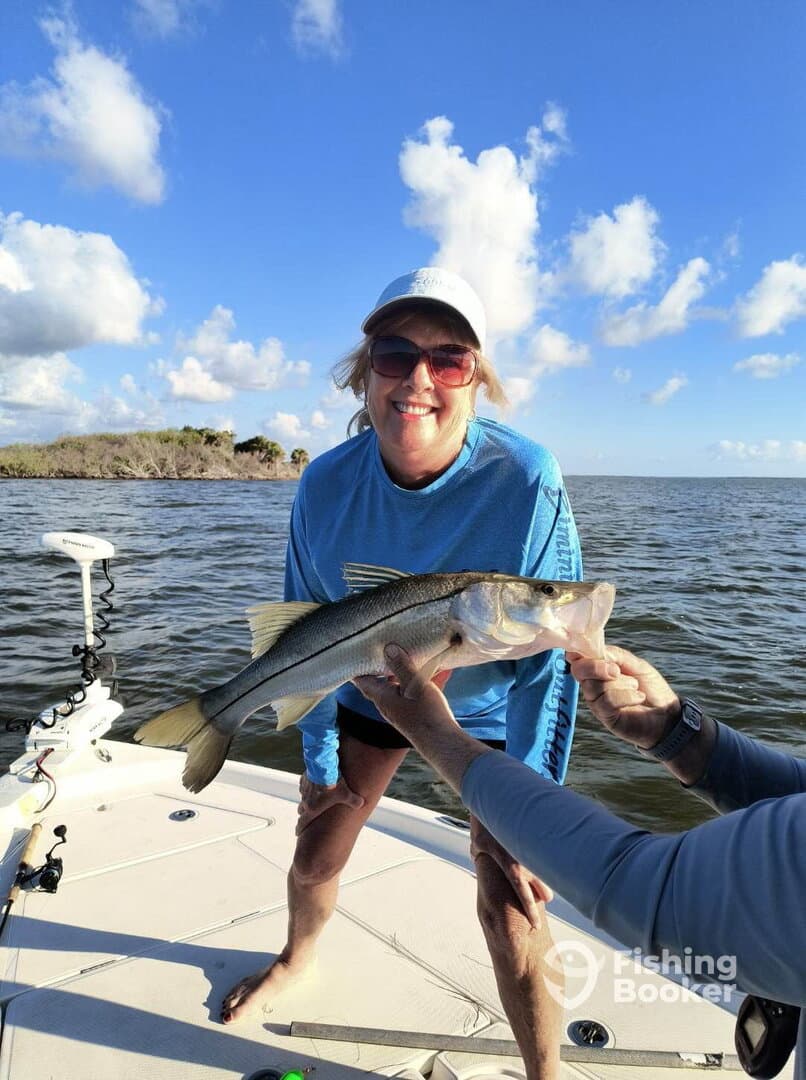 A smiling angler proudly displays a Snook while fishing on a sunny day, showcasing the joy of a successful catch.