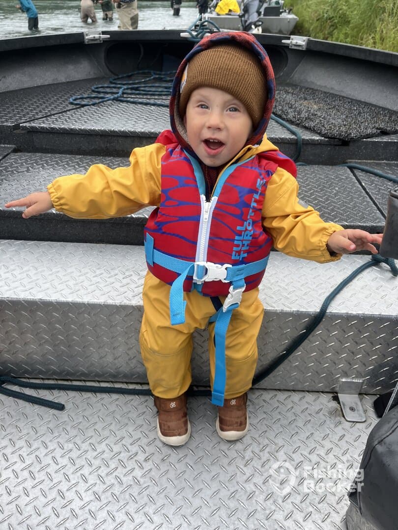 A young child in a colorful life jacket is excitedly posing on a fishing boat, showcasing the fun of a family fishing trip.