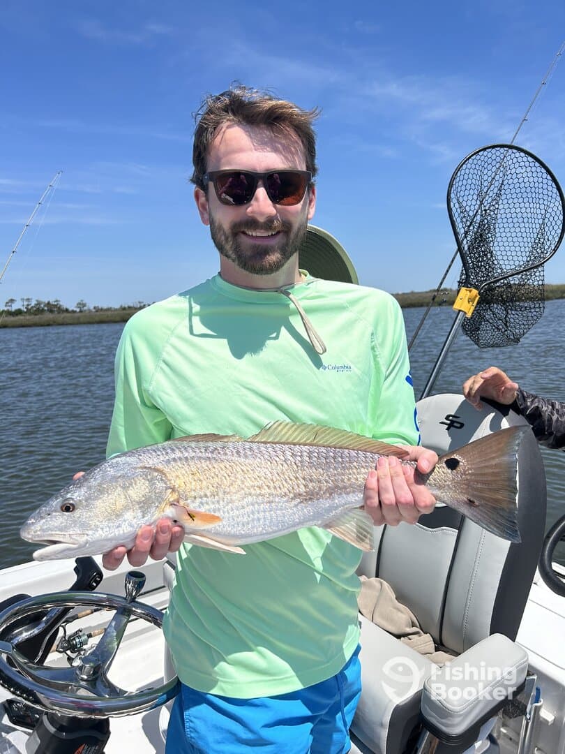 Angler proudly displaying a large Redfish while fishing in a scenic coastal environment.