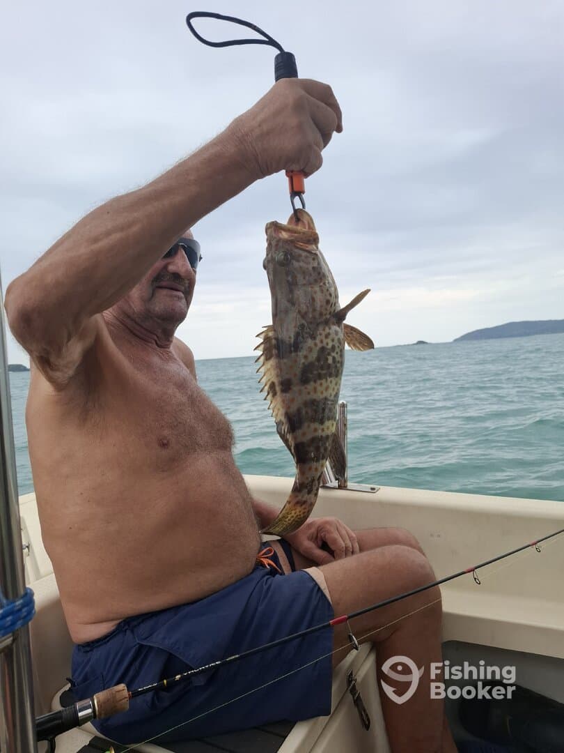 An angler proudly displaying a large Grouper while fishing from a boat in calm waters.