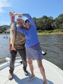 A couple proudly displaying a large Redfish while enjoying a sunny day on the water.