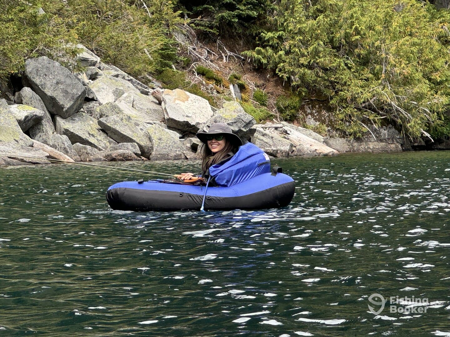 A female angler enjoying a peaceful fishing experience in a blue inflatable boat surrounded by rocky terrain and lush greenery.