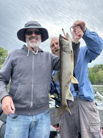 Two anglers proudly displaying a large Lake Trout while fishing on a scenic lake.