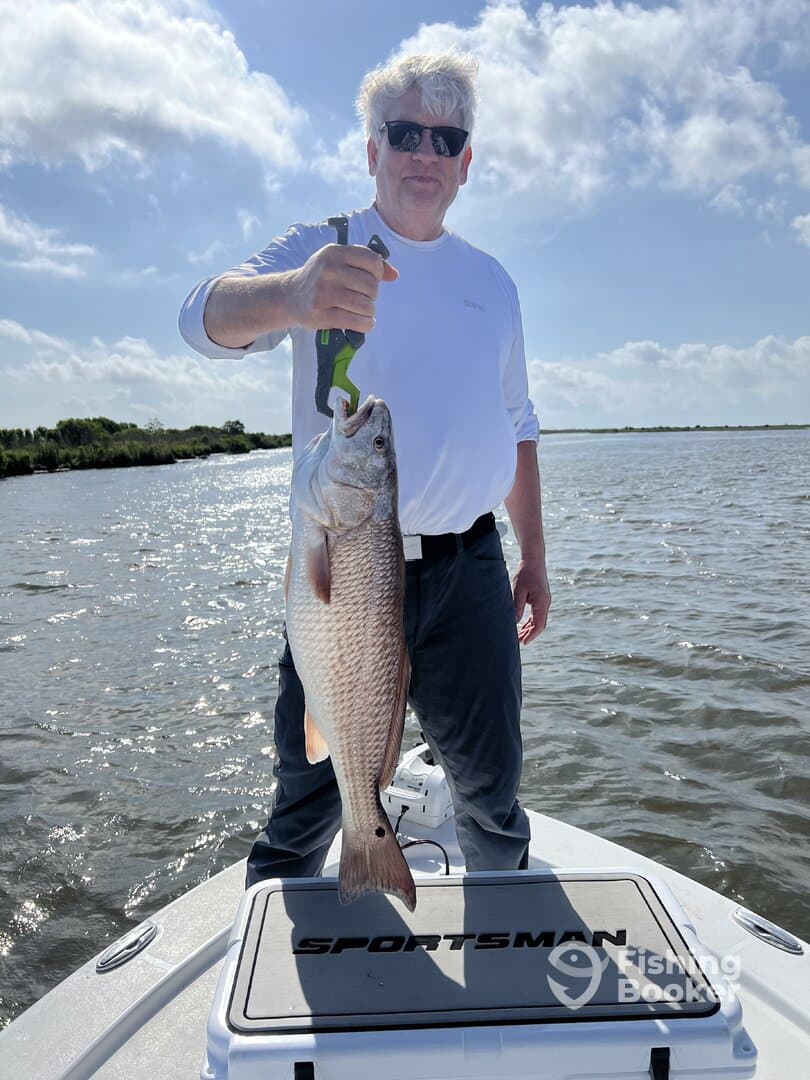 Angler proudly displaying a large Redfish while standing on a Sportsman boat in a scenic waterway.