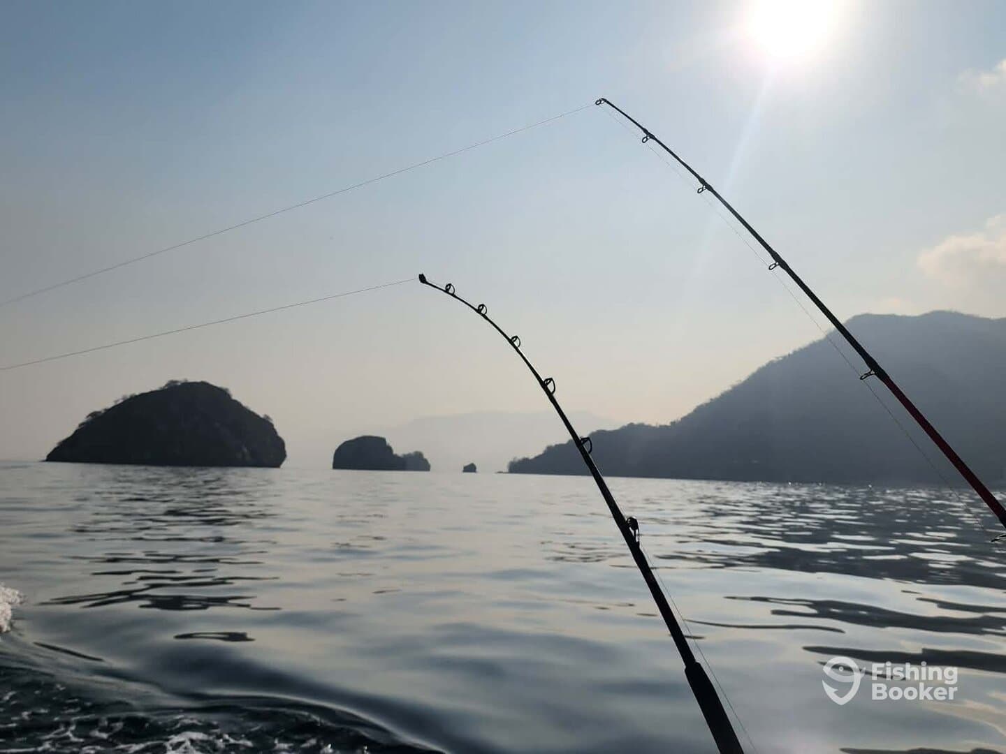 Fishing rods are positioned over calm waters, with scenic islands in the background, indicating an active fishing environment.