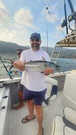 Angler proudly displaying a Bonito while fishing on a boat, with scenic mountains in the background.