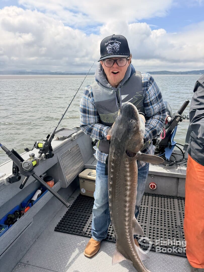 Excited angler holding a large Sturgeon on a fishing boat, showcasing a successful catch during a day on the water.