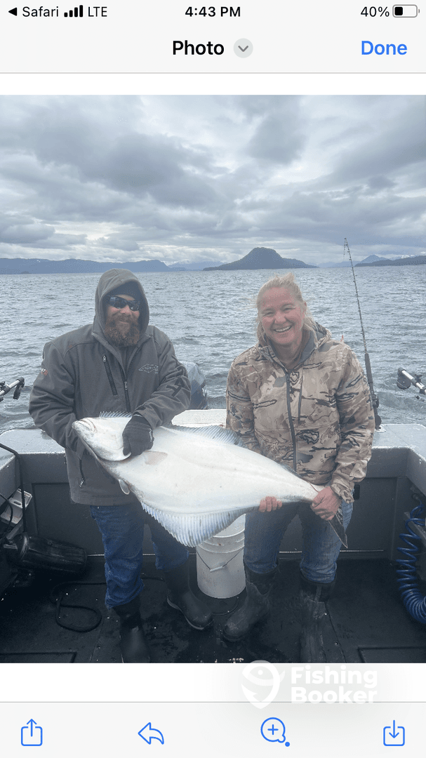 Two anglers proudly displaying a large Halibut on a fishing boat, showcasing their successful catch during a fishing trip.