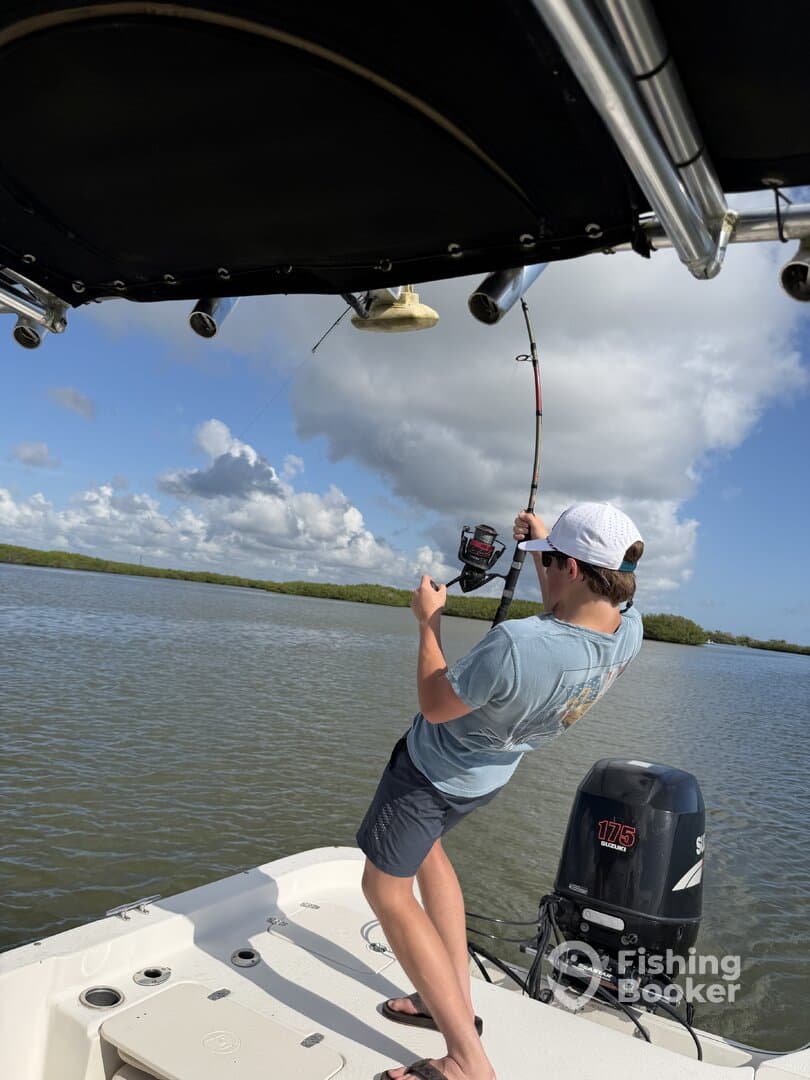 A young angler is actively reeling in a fish from a boat in a scenic mangrove setting, showcasing the excitement of fishing in a coastal environment.