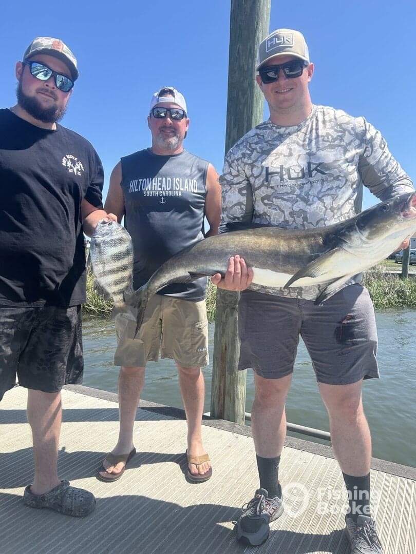 Three anglers proudly displaying their catch, including a large catfish and a flounder, at a dock in Hilton Head, South Carolina.
