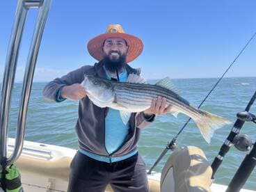 Angler proudly displaying a large Striped Bass while fishing on a sunny day.