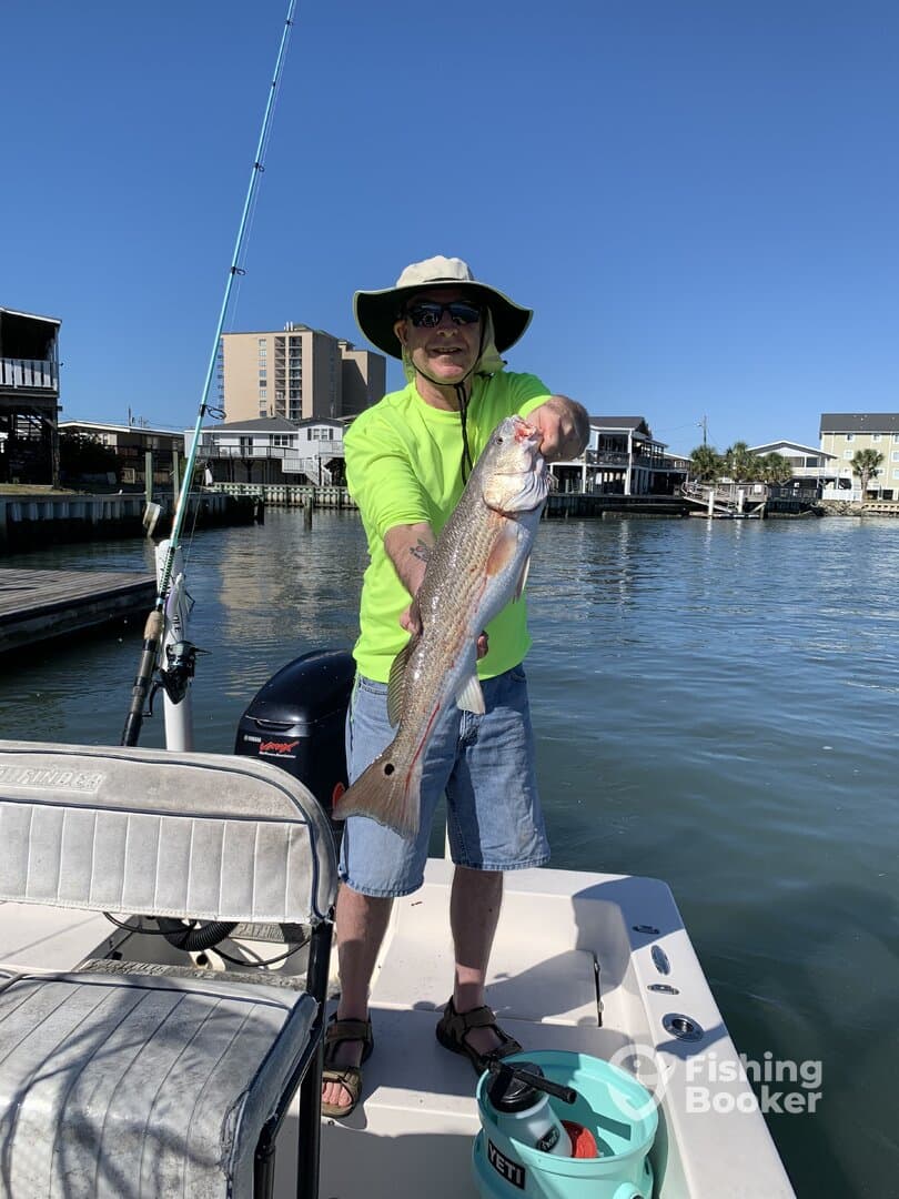Angler proudly displaying a large Speckled Trout while fishing from a boat in a coastal waterway.