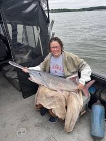 A proud angler holding a large catfish while seated on a fishing boat, showcasing a successful catch during a freshwater fishing trip.