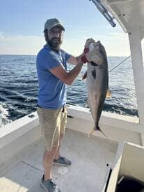 Angler proudly displaying a large fish while aboard a fishing boat in open waters.