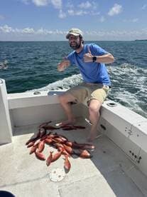 A happy angler giving a thumbs up next to a pile of freshly caught Red Snapper on a fishing boat in sunny waters.