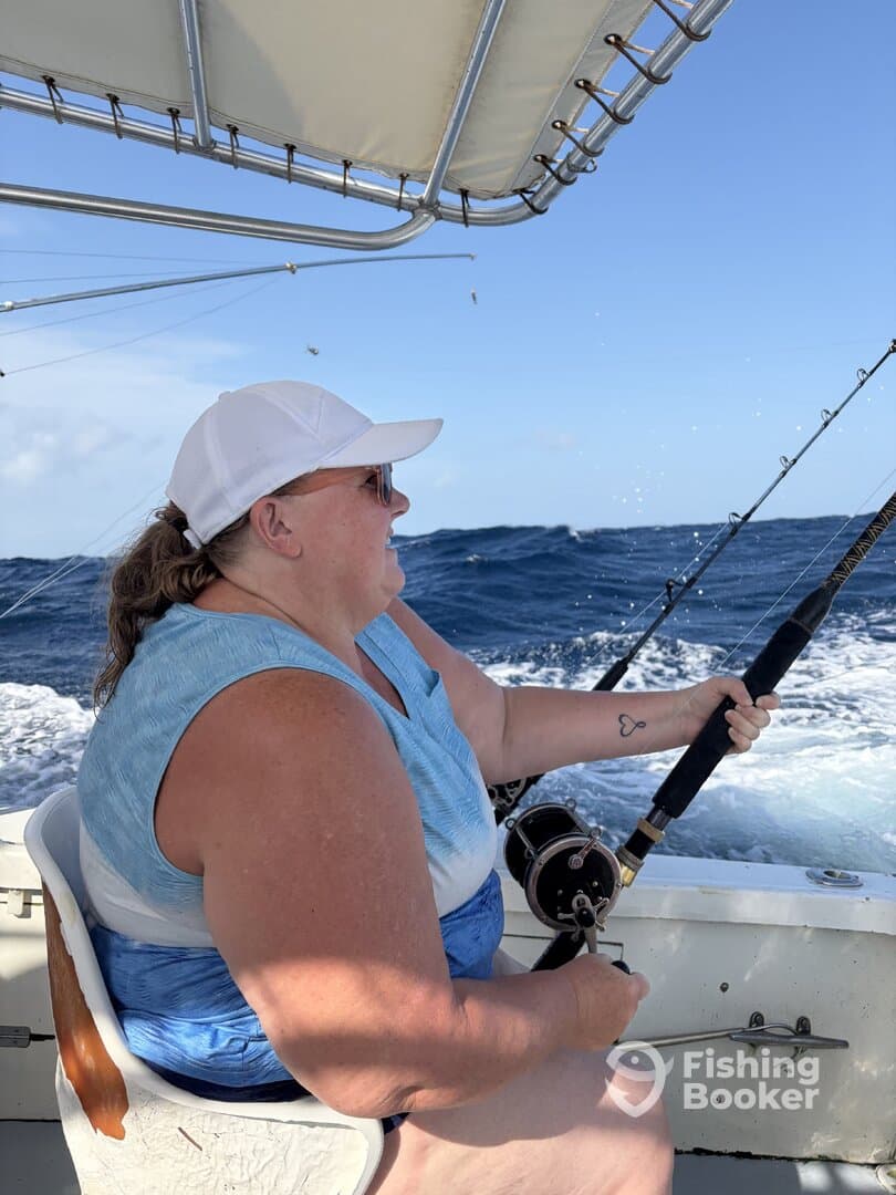 A woman actively reeling in a fish while fishing on a boat in open waters, showcasing the excitement of deep-sea fishing.