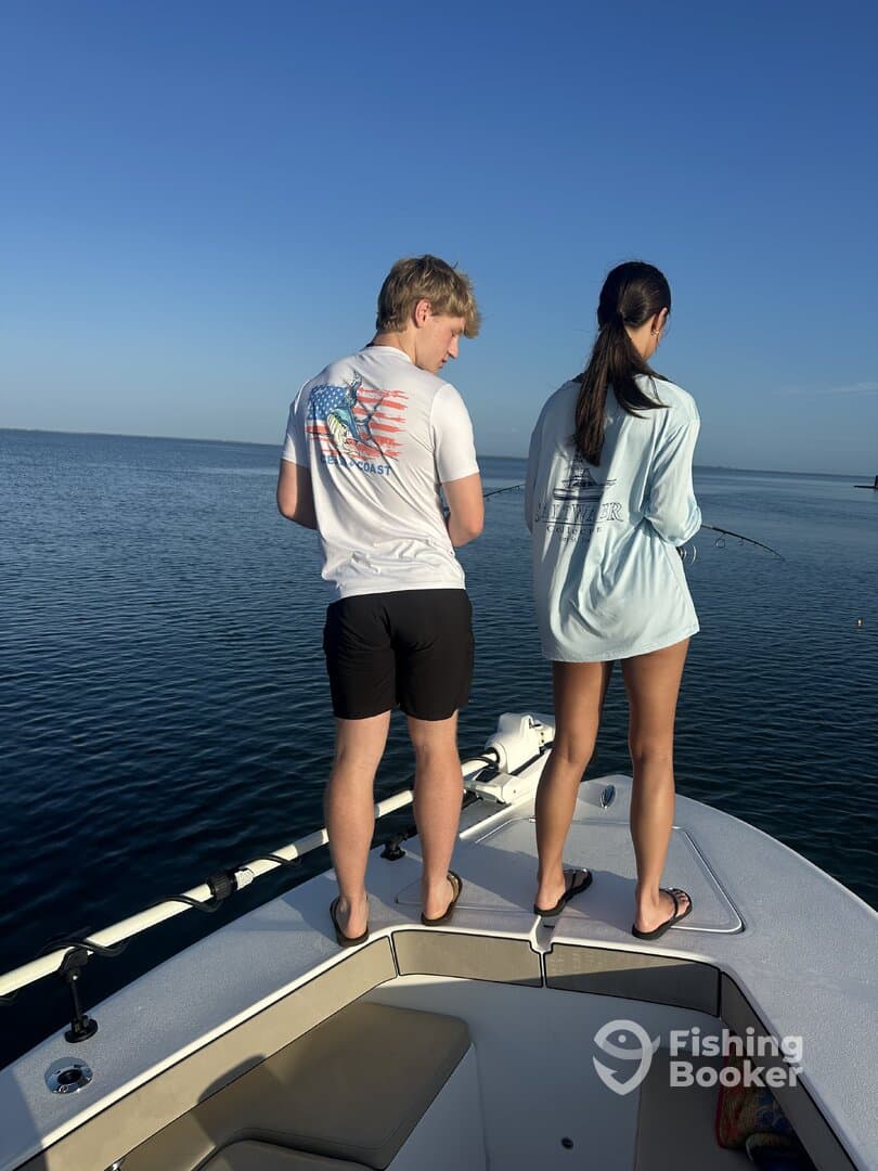 Two young anglers fishing from the bow of a boat in calm waters, enjoying a sunny day on the water.