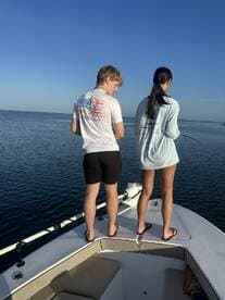 Two young anglers fishing from the bow of a boat in calm waters, enjoying a sunny day on the water.